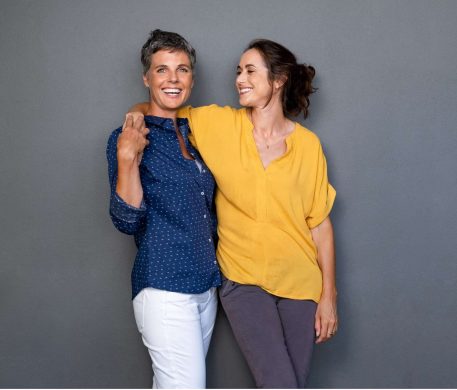 iStock-1180926158-min-2048x1588-1 two women with their arms around each other. One is smiling at the other, the other is smiling at the camera.